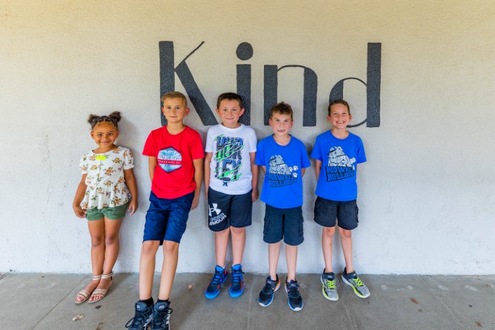 Student's standing in front of a wall with the word kind painted on it.